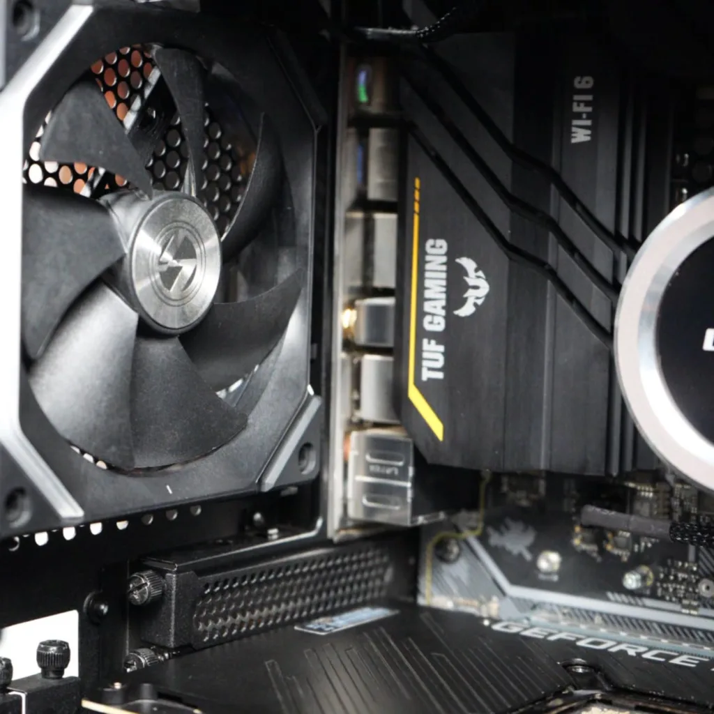 Inside a gaming PC, showing the rear cooling fan, TUF Gaming motherboard, and GeForce graphics card.
